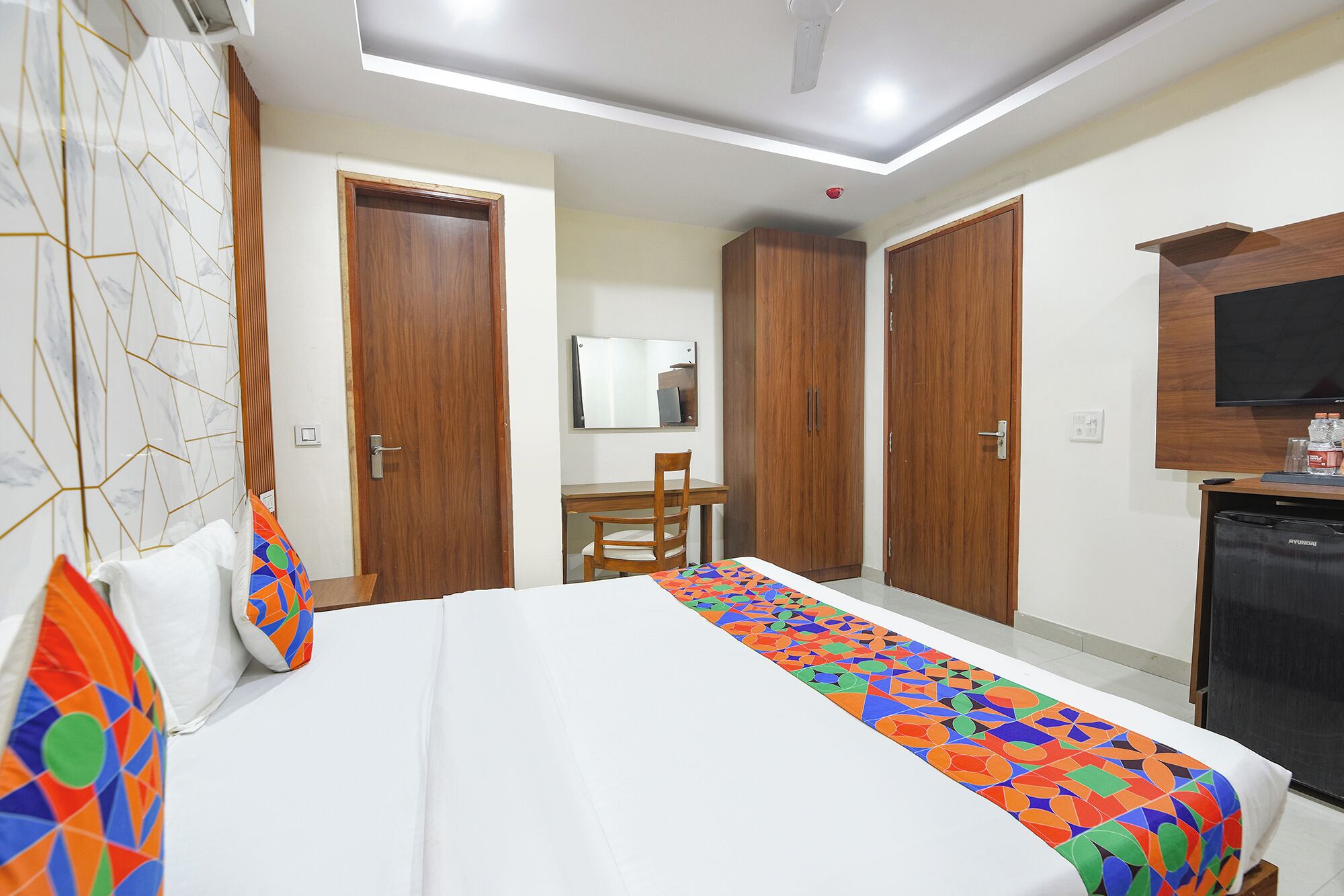 Una habitación de hotel con cama, escritorio, silla, armario y televisor.