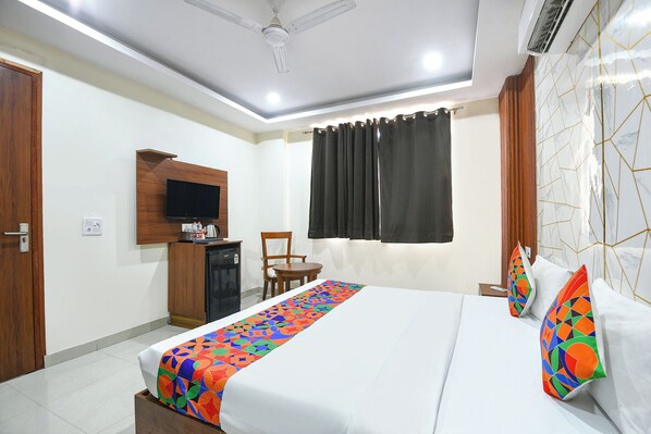 A hotel room with a bed, a desk, a chair, a television, and a window with curtains. - Fabhotel Laxmi Mahal (New Delhi)