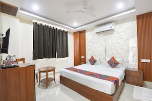 A hotel room with a bed, bedside tables, a desk with a chair, a television, and an air conditioning unit. - Fabhotel Laxmi Mahal (New Delhi)