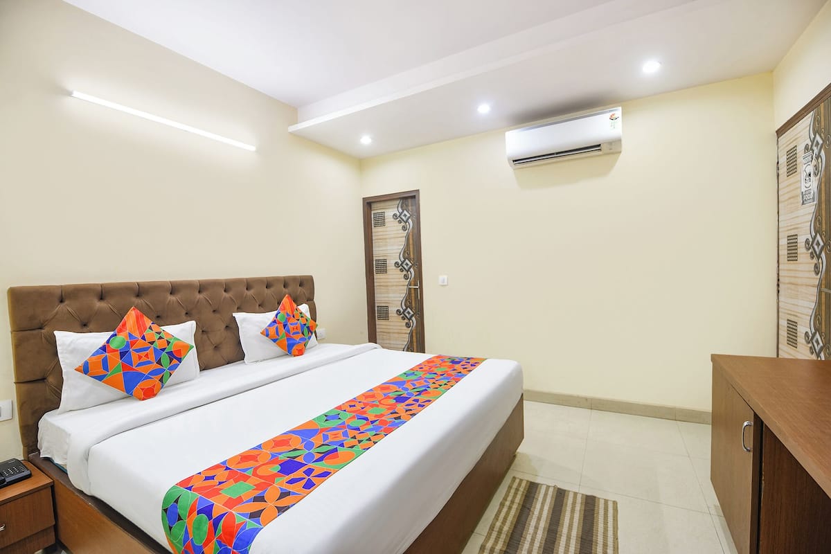 A hotel room with a tufted headboard, a bed with colorful geometric pillows, a white bedspread, and a striped rug.