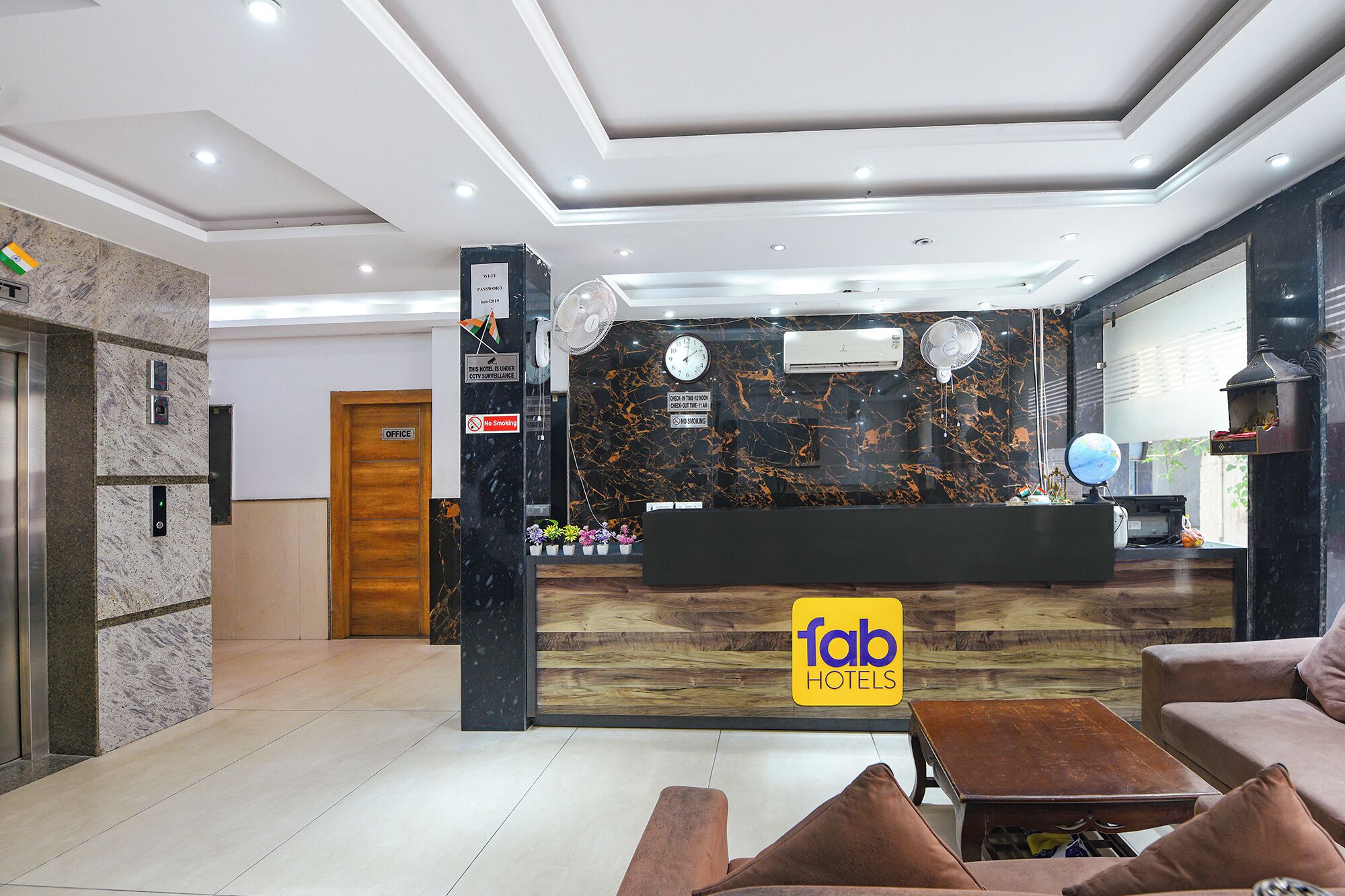 A hotel reception area with a marble reception desk, a clock, and a sign indicating the hotel is under CCTV surveillance.