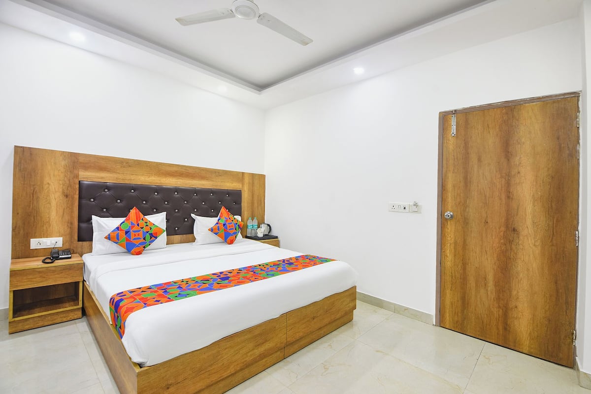 Habitación de hotel con cabecera de madera, cama con ropa blanca, almohadas coloridas, mesita de noche y ventilador de techo.