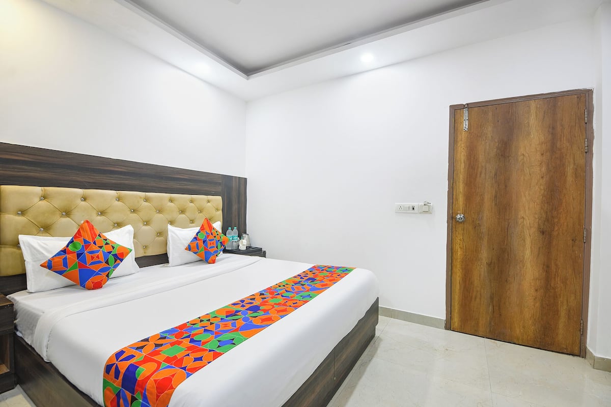 Una habitación de hotel con un cabecero capitonado, una puerta de madera y una cama con un edredón de diseño geométrico y colores vivos.