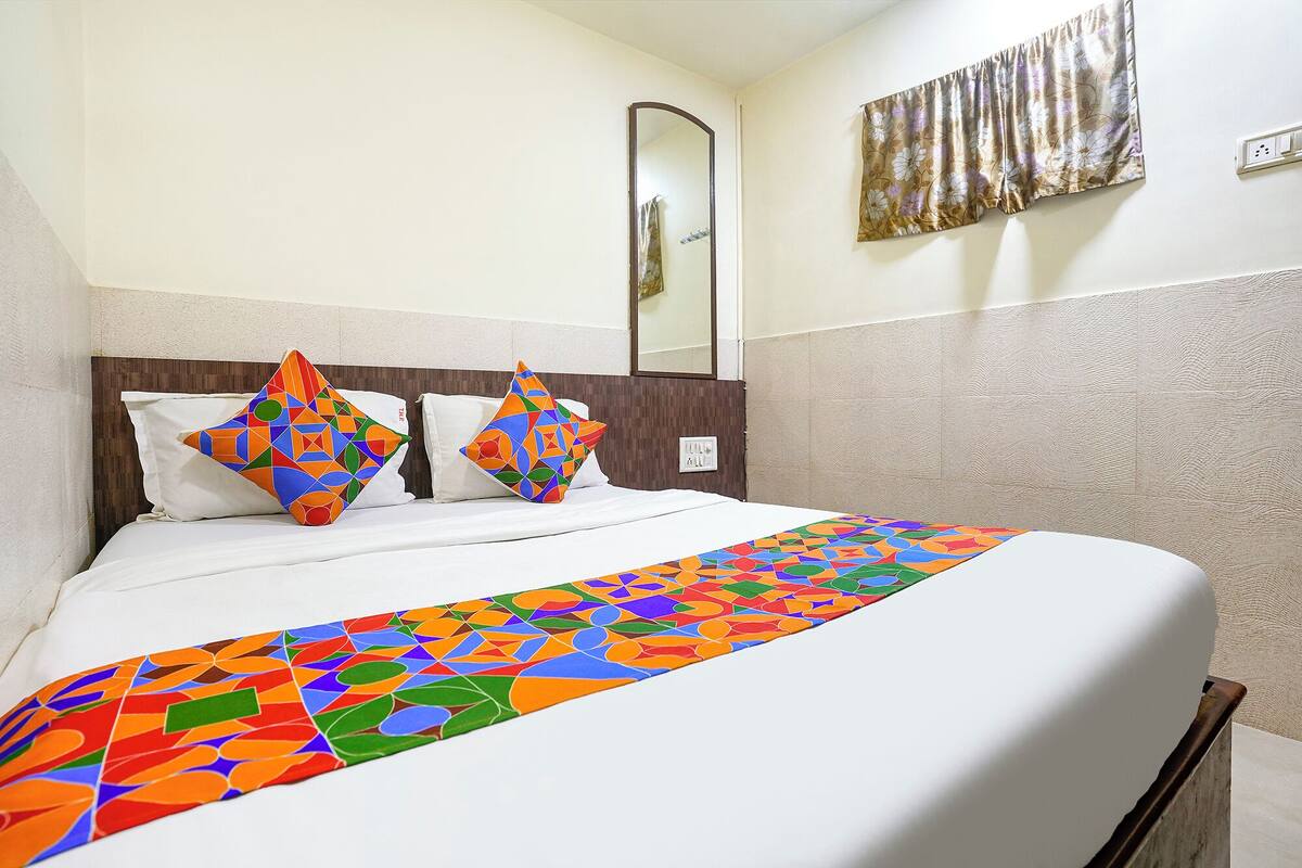 A hotel room with a neatly made bed, a large mirror, and a floral-patterned curtain.