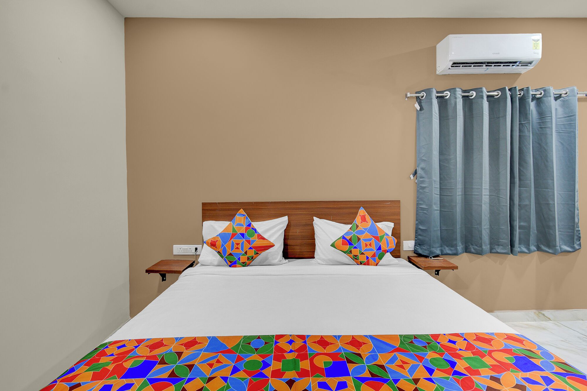 A bedroom with a bed, two pillows, a nightstand, an air conditioning unit, and a window with curtains.