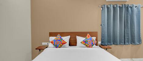 A bedroom with a bed, two pillows, a nightstand, an air conditioning unit, and a window with curtains.
