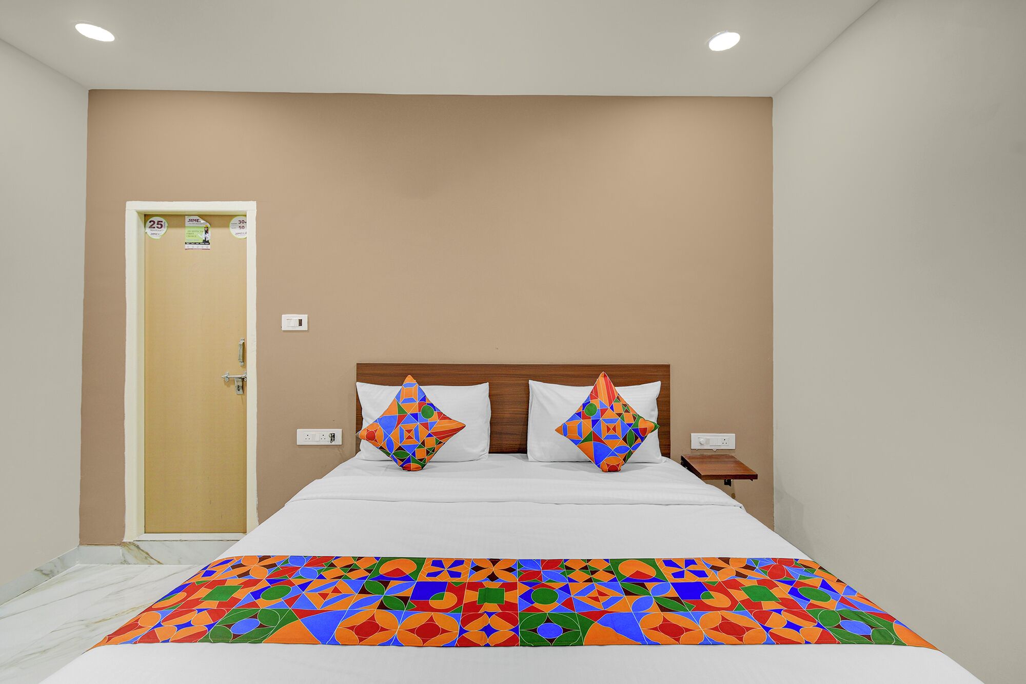 A hotel room with a bed, two pillows, a nightstand, and a door.