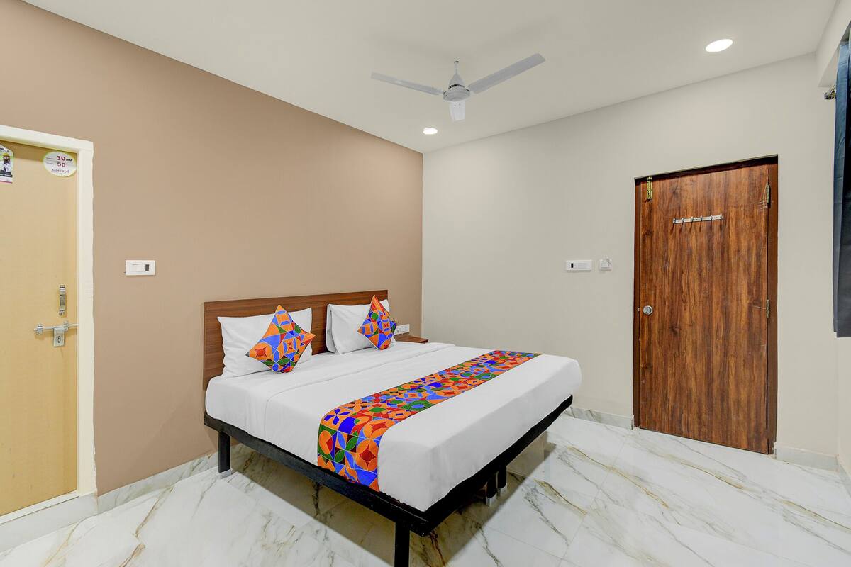 A hotel room with a bed, a ceiling fan, a wooden door, and a marble floor.