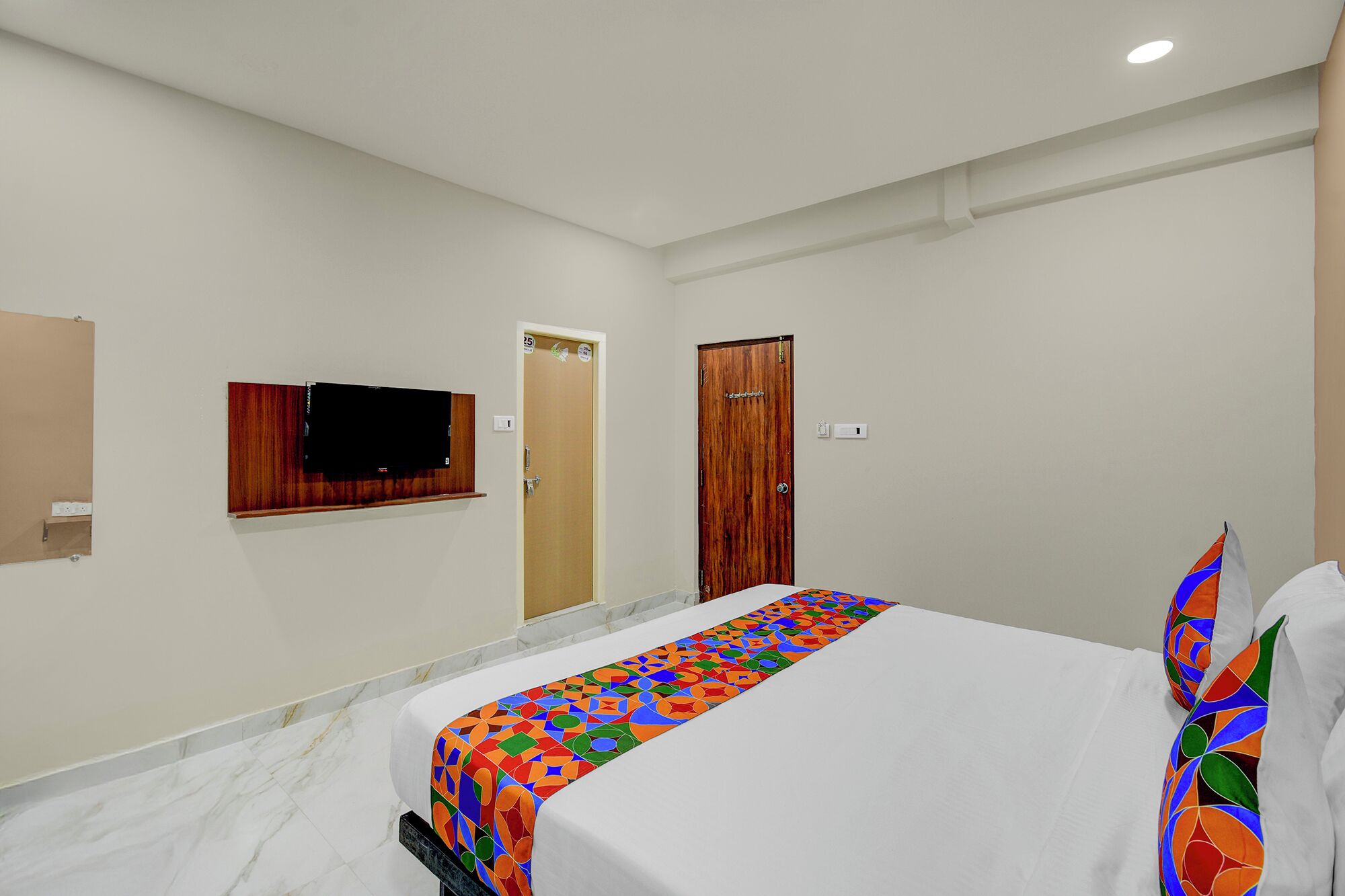 Una habitación de hotel con una cama, un televisor montado en la pared, una puerta de madera y una pared blanca.