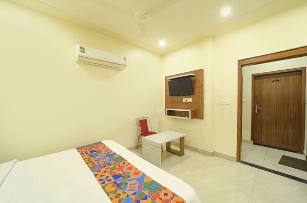 A hotel room with a bed, a small desk, a TV mounted on the wall, and a door with a number.
