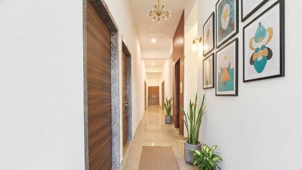 A hallway with a wooden door, a potted plant, and framed artwork on the wall. - FabHotel Shree Radhey Shyam Palace - 500m Khatushyam Temple Khatoo (Khatoo)