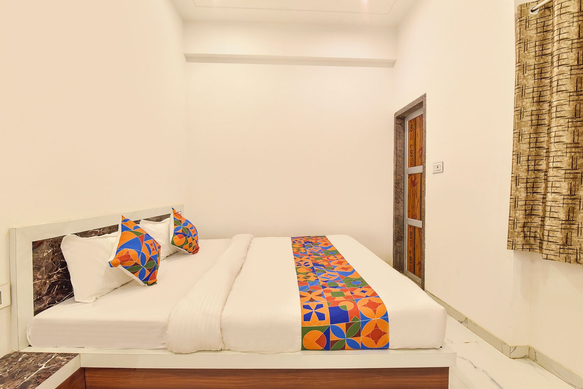 A single bed with a white mattress, two pillows, and a colorful geometric-patterned bedspread.