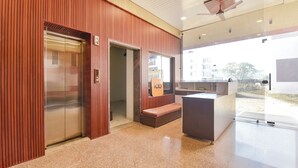 A hotel reception area with a wooden panel wall, a reception desk, a bench, and an elevator. - FabHotel Shree Radhey Shyam Palace - 500m Khatushyam Temple Khatoo (Khatoo)