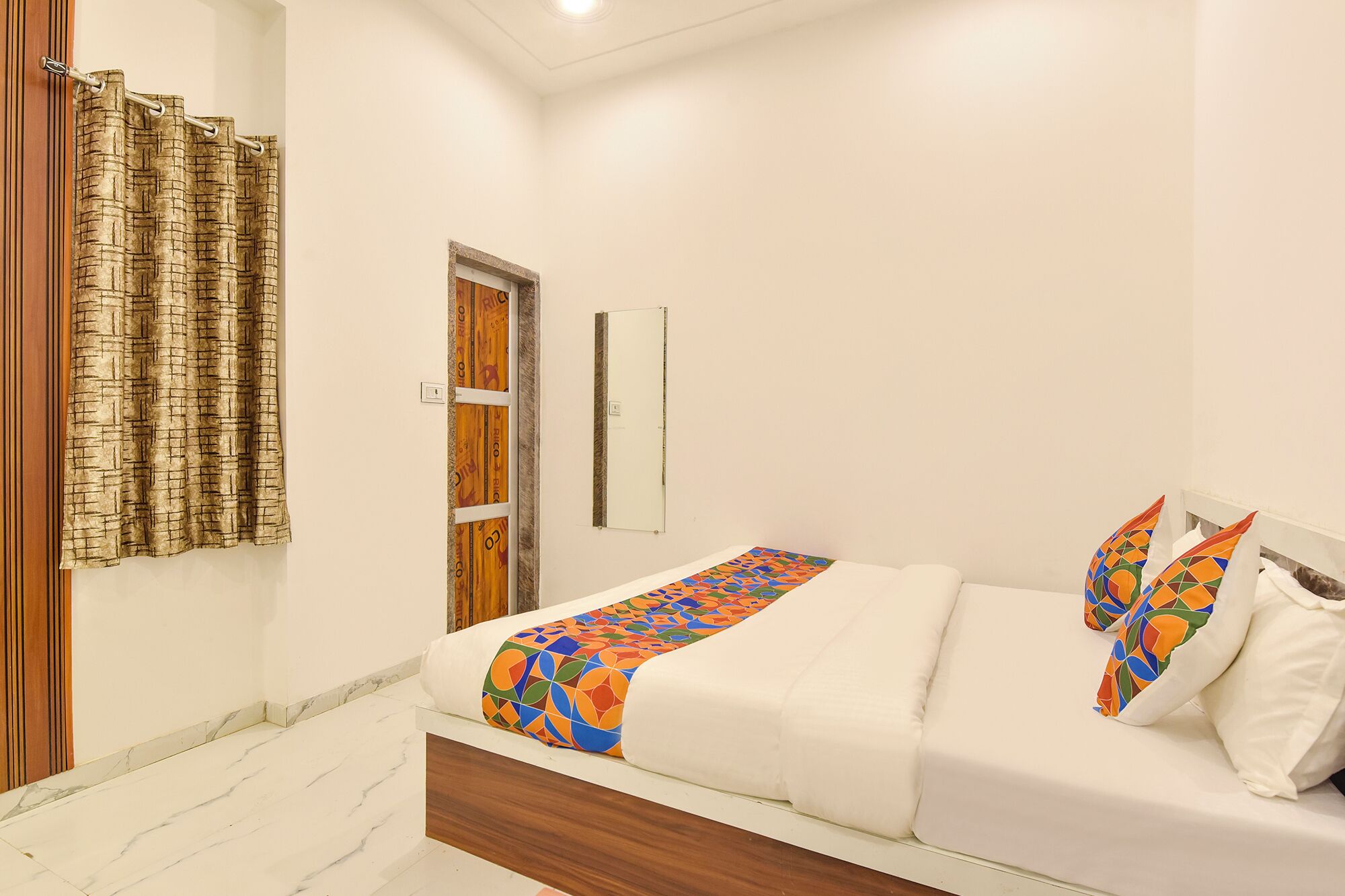 A bedroom with a bed, a wooden door, a mirror, and a curtain.