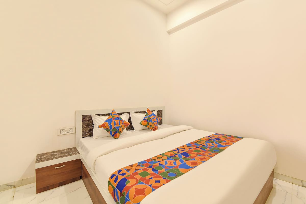 A neatly made bed with a geometric-patterned bedspread and pillows, a wooden nightstand with a drawer, and a marble-patterned floor.