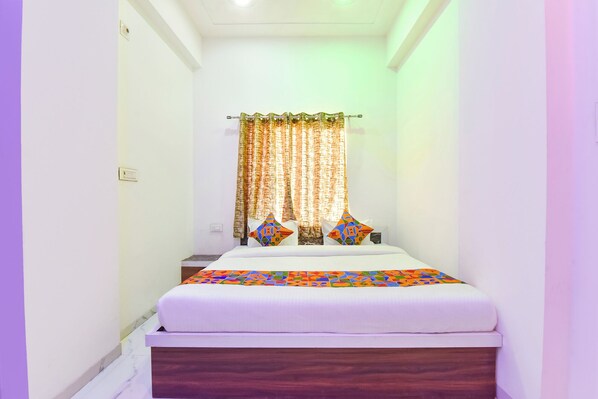 Una habitación de hotel estrecha con una cama, una mesita de noche y un ventanal con cortinas.