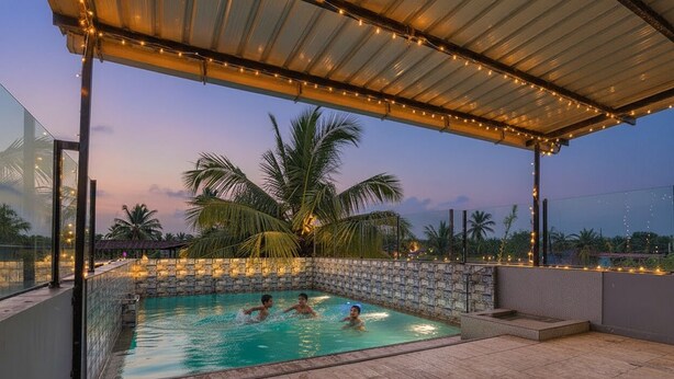 An outdoor swimming pool with a stone wall and palm trees in the background. - Fabhotel Beach Front Resort (Calangute)