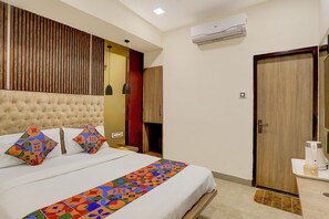 A hotel room with a tufted headboard, a bed with colorful geometric pillows, a patterned runner, a wooden door, and a coffee machine on the side table. - FabHotel Beach Front Resort (Calangute)