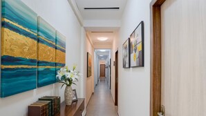 A hallway with artwork on the walls, a wooden console table with books and a vase, and a door at the end. - Fabhotel Beach Front Resort (Calangute)