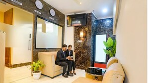A reception area with a sofa, a potted plant, a clock, and a TV. - Fabhotel Melody Nx (Thane)