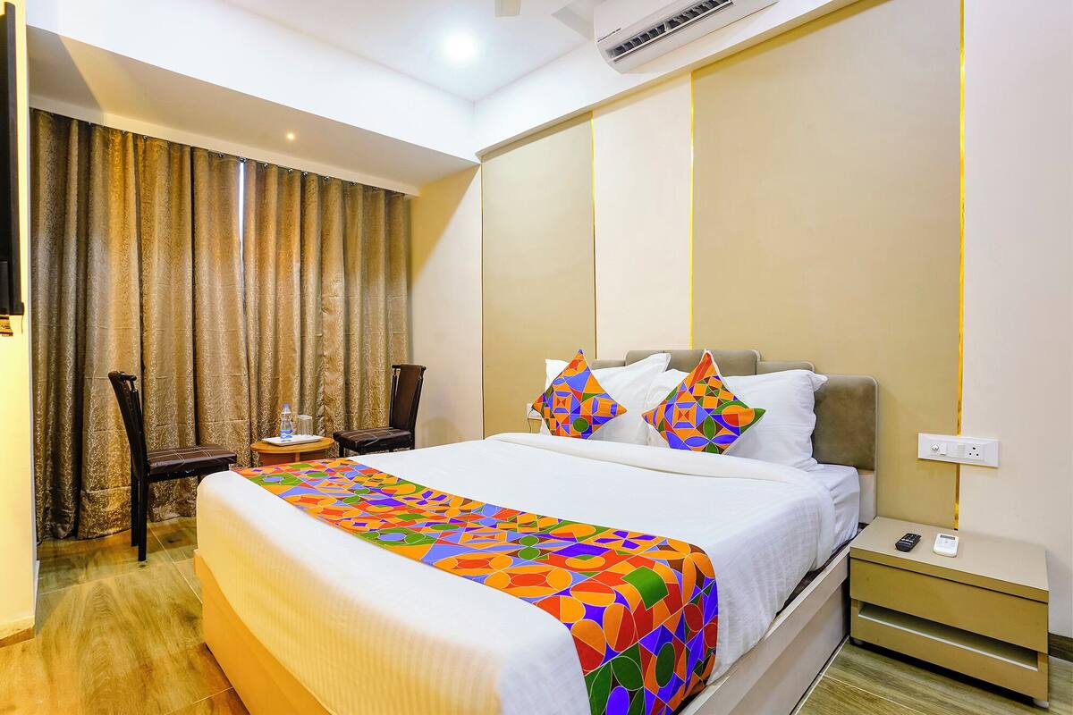 A hotel room with a bed, a chair, a nightstand, and a window with curtains.