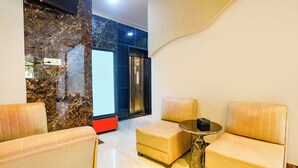 A modern lobby with marble walls, a glass elevator, and two leather armchairs with a small table. - Fabhotel Melody Nx (Thane)