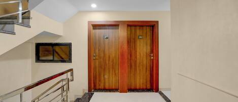 Un pasillo de hotel con una escalera, dos puertas de madera con la indicación 201 y 202, y un candelabro.