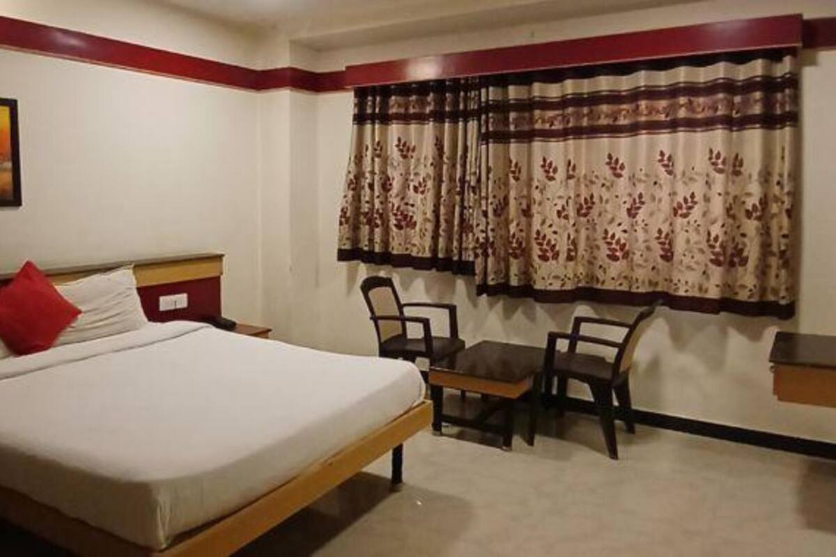 A hotel room with a bed, two chairs, a small table, and a painting on the wall.