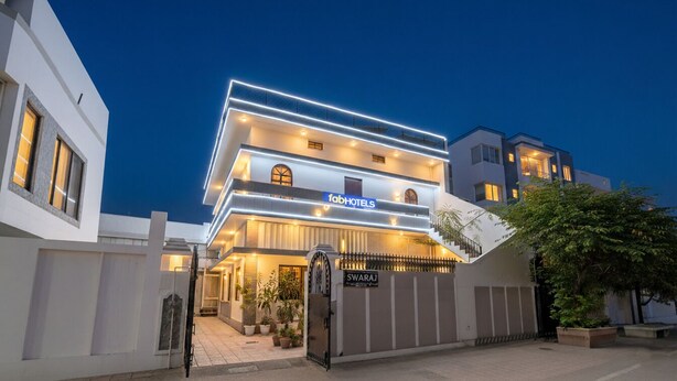 Un hôtel moderne avec une façade à plusieurs étages, une entrée sécurisée par un portail et une enseigne portant le nom « Swaraj ».