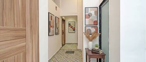 Un couloir doté d’un sol à motifs, de tableaux encadrés accrochés aux murs et d’une petite table ornée d’objets décoratifs.