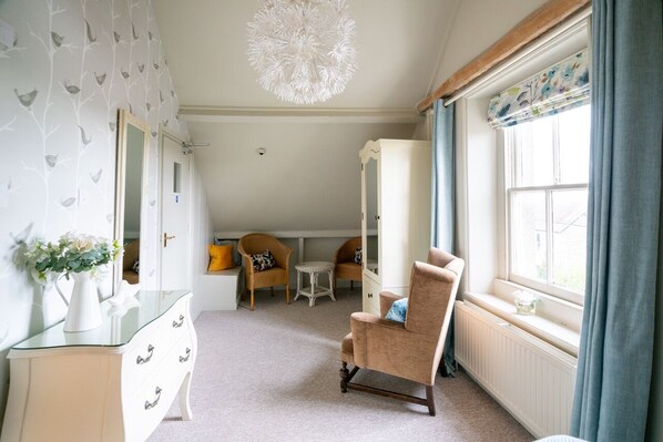 A room with a glass dresser, a chair, a small table, and a window with curtains.