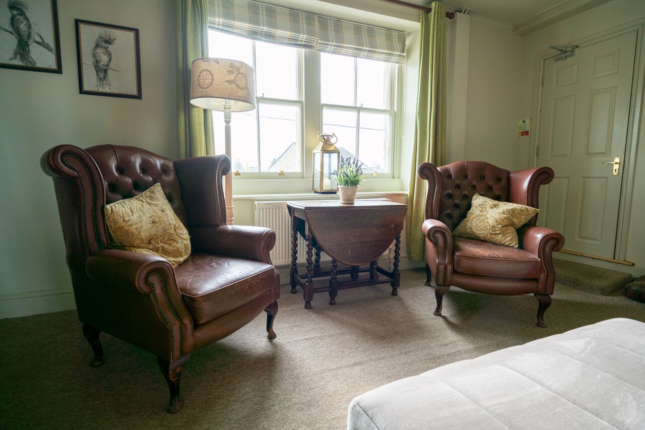 A room with two leather armchairs, a small table with a lamp, and a window with curtains.