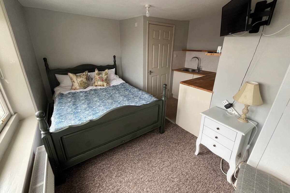 Un dormitorio con cama, un escritorio pequeño, televisor y ventana.