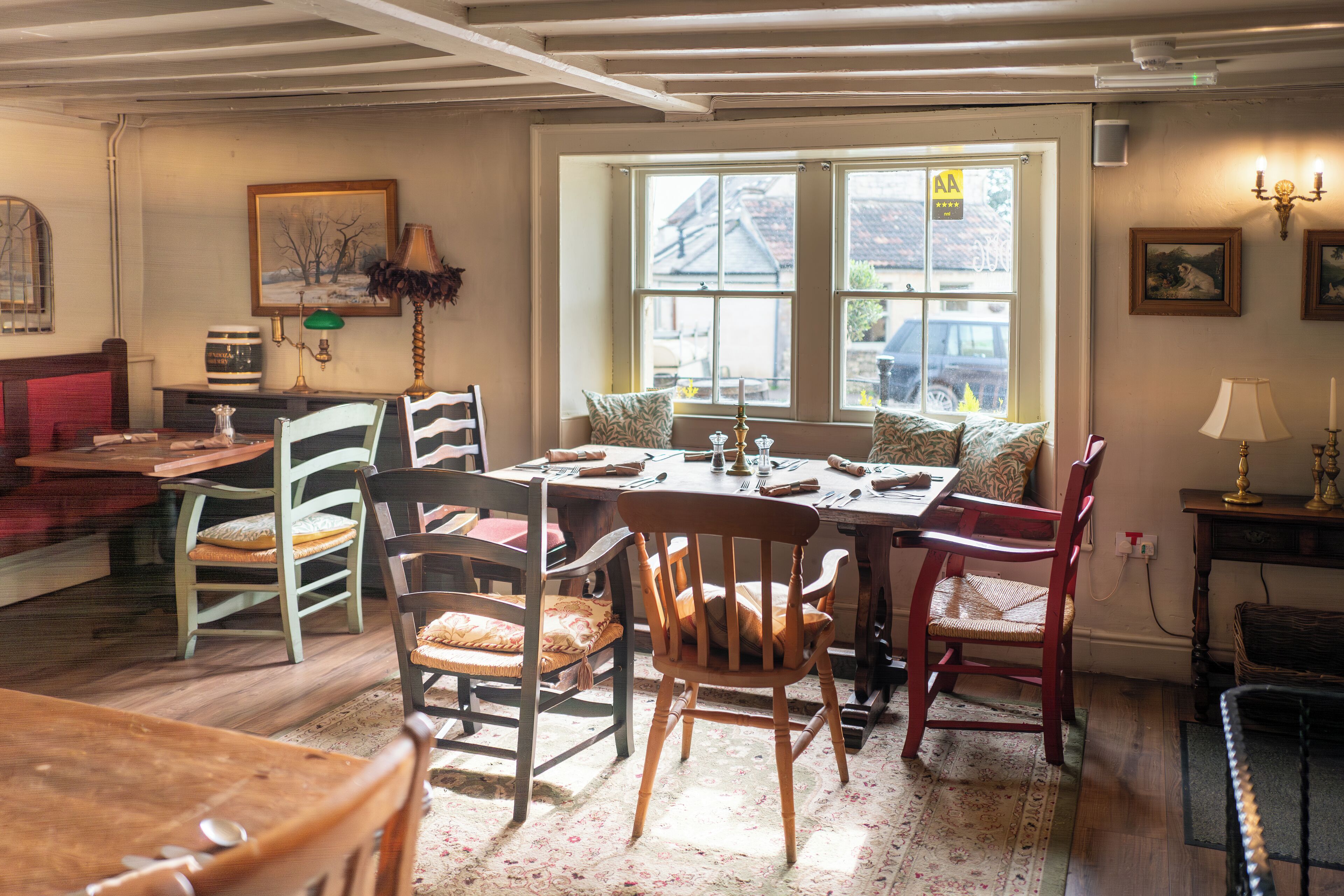 Un coin repas avec une table et des chaises en bois, une fenêtre donnant sur l’extérieur et un tableau accroché au mur.