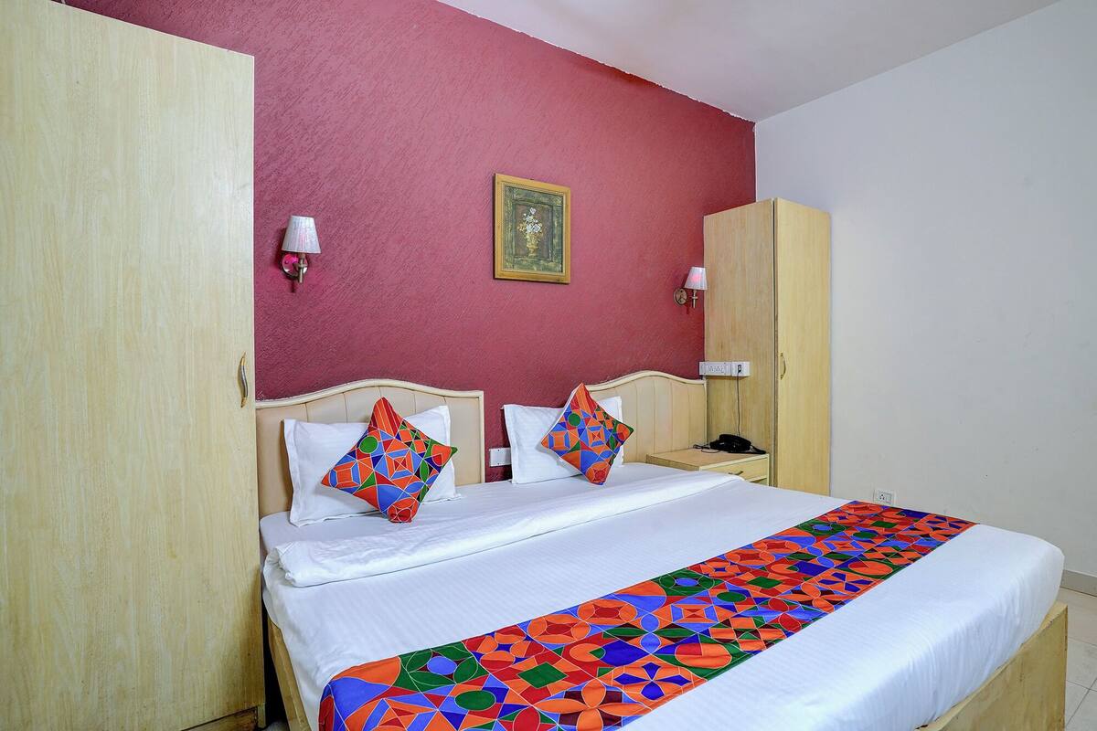 A hotel room with a bed, two pillows, a bedside table, a lamp, and a wardrobe.