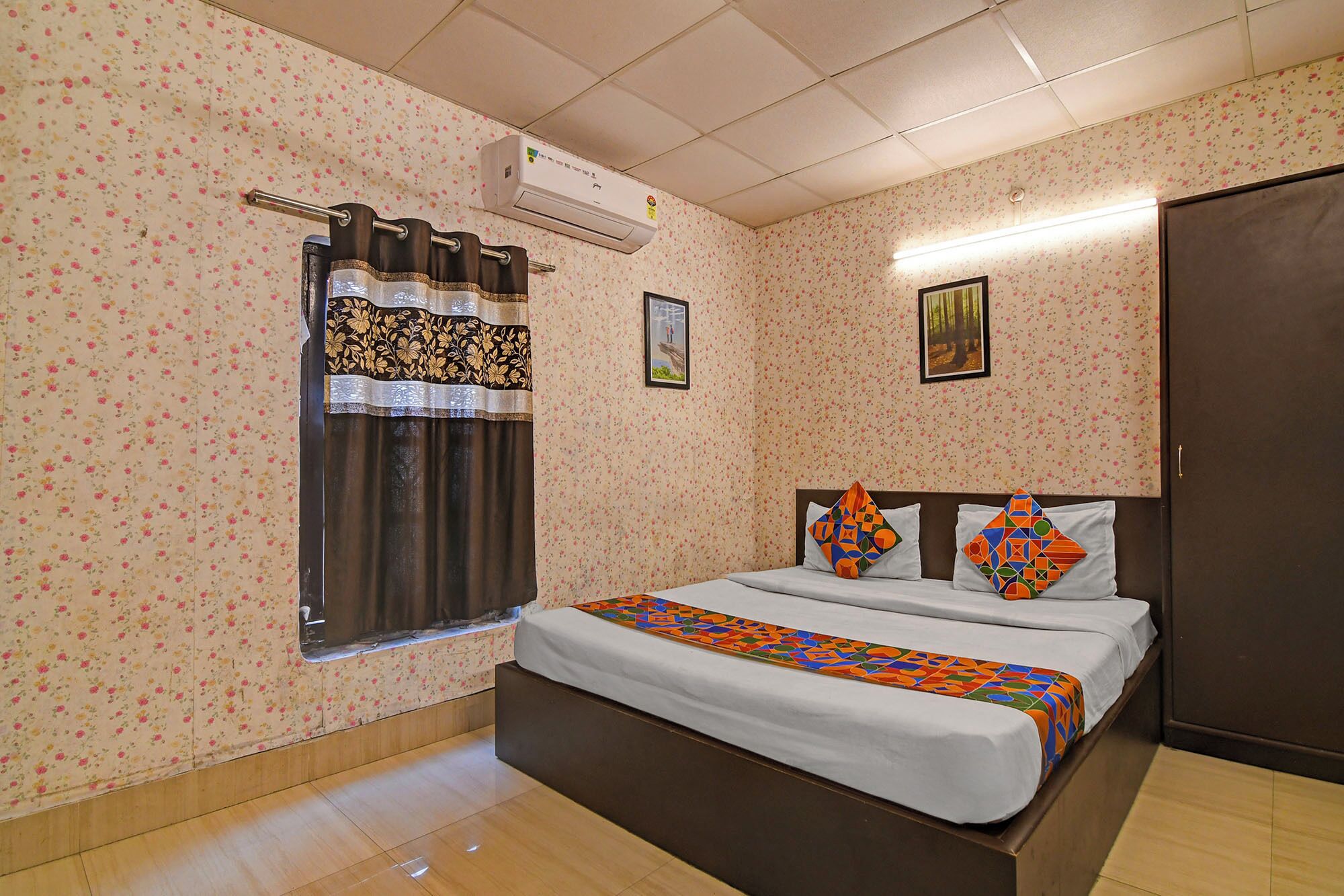 Un dormitorio con papel tapiz floral, una cama con almohadas estampadas, una ventana con cortinas y un equipo de aire acondicionado.