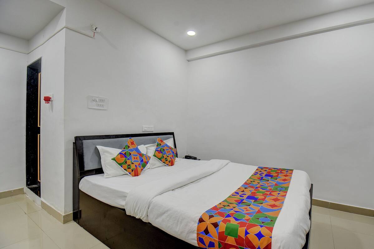 A neatly made bed with a colorful geometric-patterned bedspread, a white pillow, and a matching pillow on a headboard.