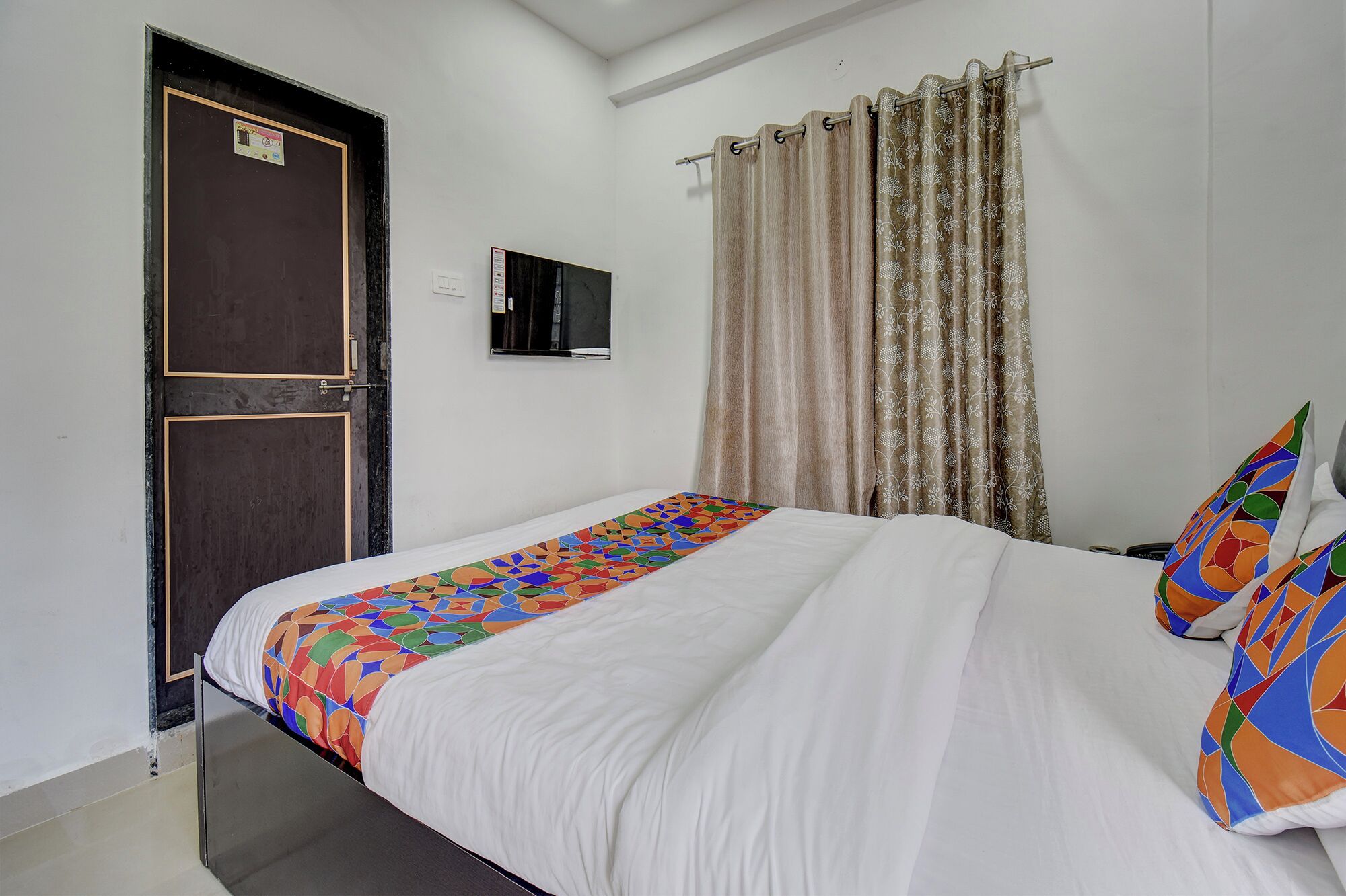 Une chambre à coucher avec un lit, une télévision, une porte et des rideaux.