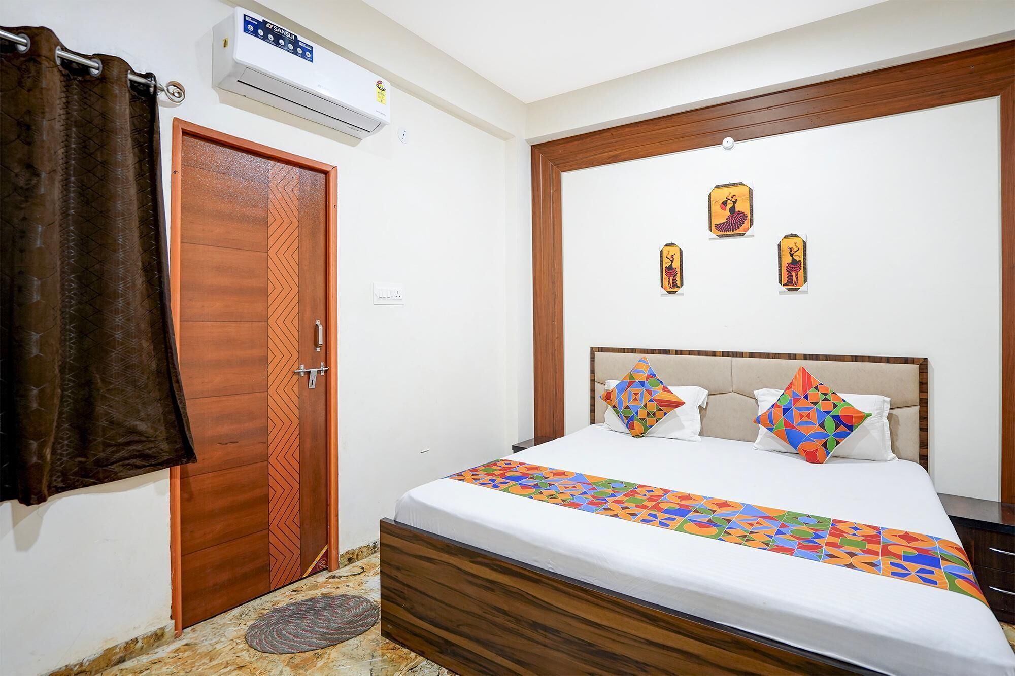Une chambre avec une porte en bois, un lit recouvert d’une couvre-lit à motifs géométriques et des œuvres d’art accrochées au mur.