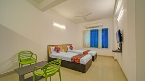 Une chambre d’hôtel avec deux lits, un bureau, des chaises, un ventilateur de plafond, un appareil de climatisation et un téléviseur.