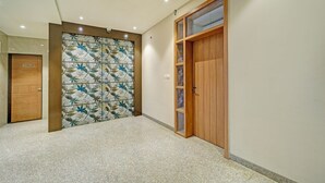 A hallway with a tiled wall, a wooden door labeled "OGENTIS," and a wooden door with a glass panel. - Fabhotel Shri Shreeyam Stay (Bhopal)