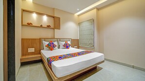 A modern hotel room with a large bed, a wooden headboard, a nightstand, a wall-mounted shelf with decorative items, and a window with a view. - Fabhotel Shri Shreeyam Stay (Bhopal)