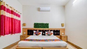 A bedroom with a bed, a headboard with a green plant, two bedside tables, and a red curtain. - Fabhotel A2 (Barasat)