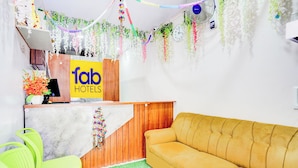 A reception area with a wooden desk, a yellow sofa, and a green chair. - FabHotel Aranya Residency - HSR Layout (Bengaluru)