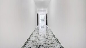 A long, narrow hallway with white walls and a marble floor. - FabHotel Aranya Residency - HSR Layout (Bengaluru)