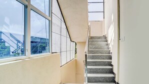 A narrow stairway with a metal railing, leading to a landing with a window overlooking greenery. - FabHotel Aranya Residency - HSR Layout (Bengaluru)