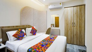 A hotel room with a bed, a nightstand, a desk, a chair, a wardrobe, and an air conditioning unit. - Fabhotel Cosmos Green (Indore)