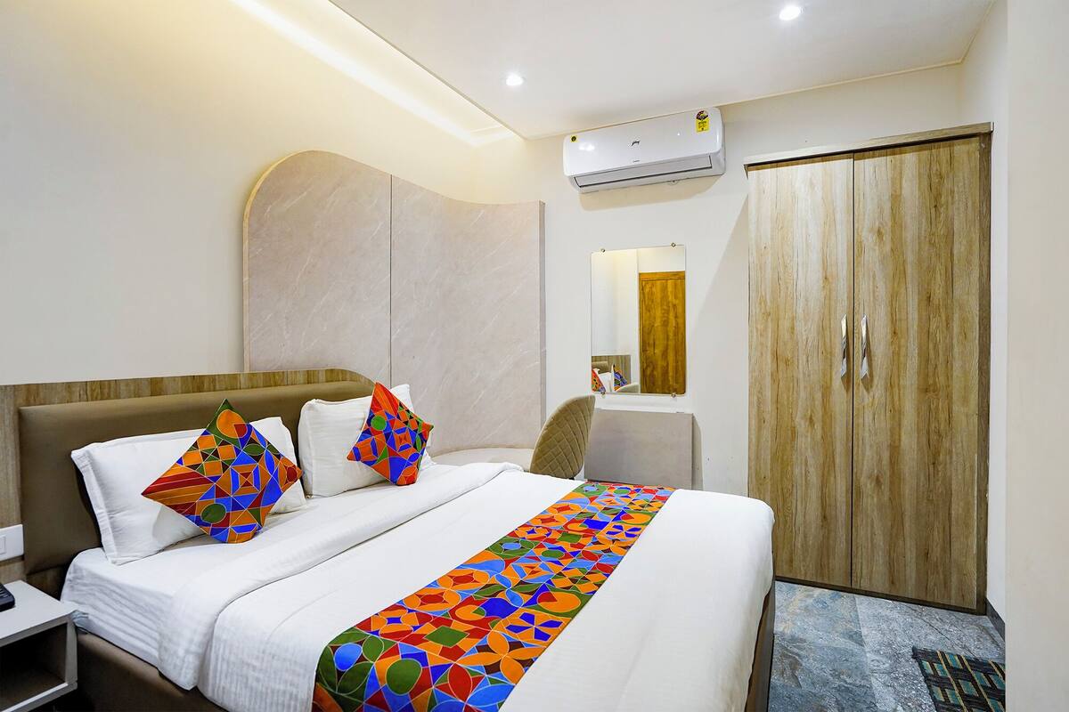 A hotel room with a bed, a nightstand, a desk, a chair, a wardrobe, and an air conditioning unit.