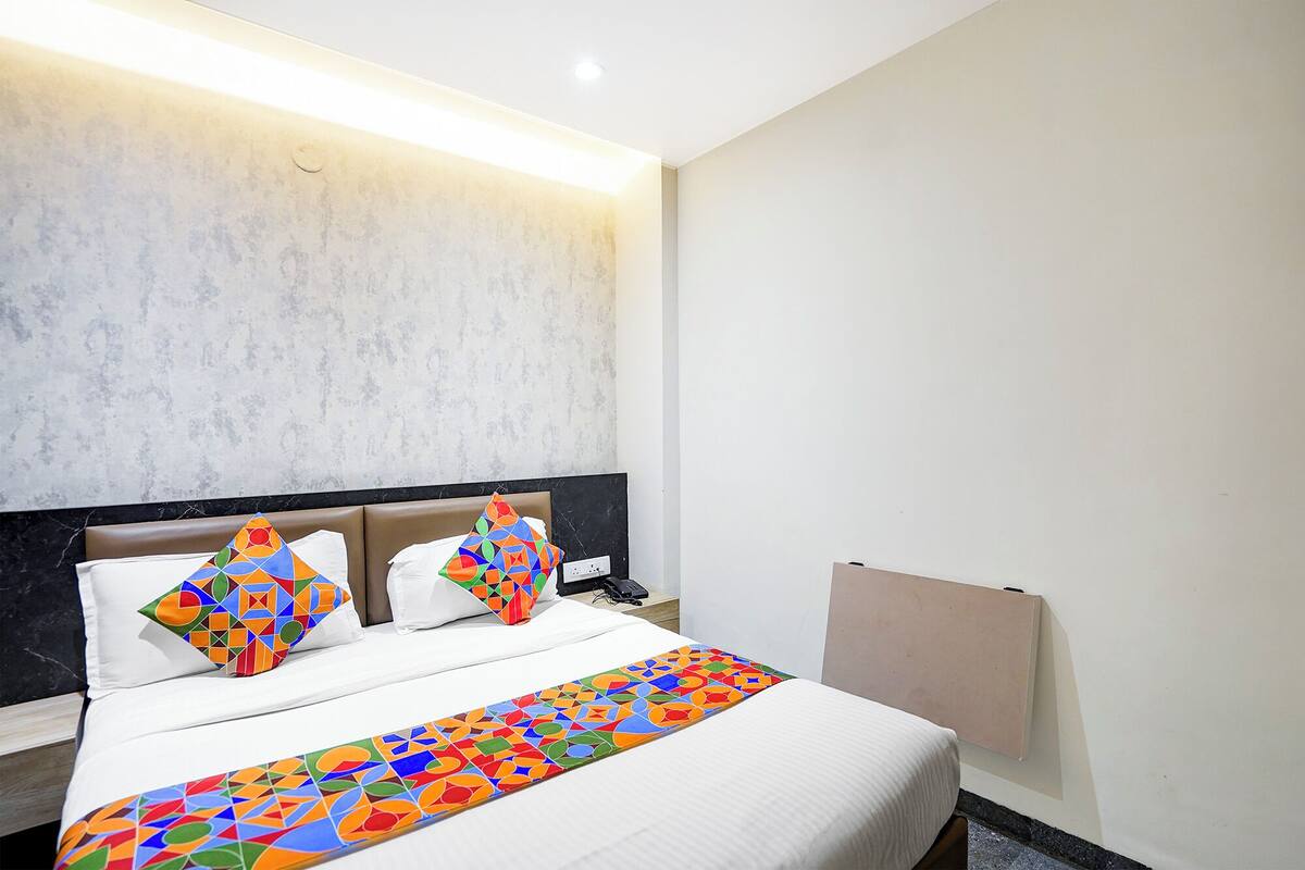 A hotel room with a bed, a headboard, a bedside table, and a wall-mounted TV.