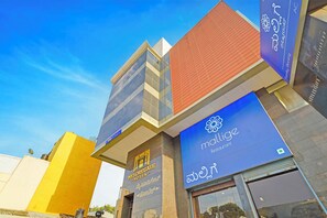 A hotel with a modern facade, a visible sign for 'MYSORE GATE HOTEL', and a prominent 'malige' restaurant sign. - FabHotel New Mysore Gate (Bengaluru)